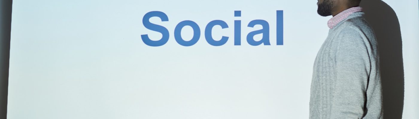 Pensive young Black SMM specialist in sweater standing at projection screen and explaining marketing plan at training class