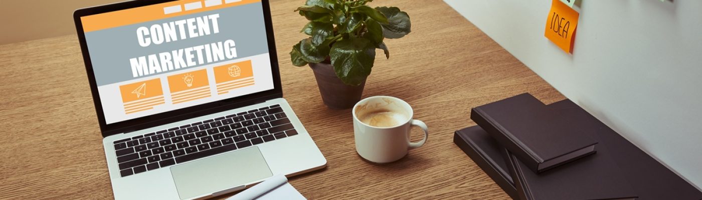 laptop with"content marketing" lettering on screen, notebooks and pencil on wooden tabletop,